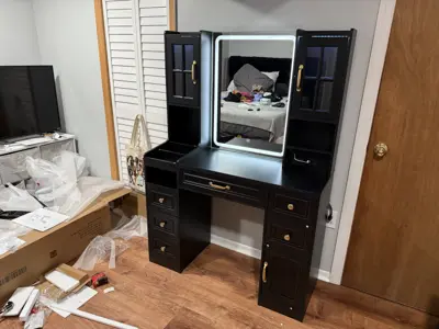 Fully assembled black vanity desk with lighted mirror and gold hardware in a NYC bedroom