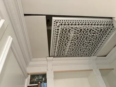 Ornate decorative ventilation screen installed on ceiling with crown molding