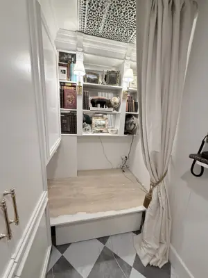 elegant built-in reading nook with white shelving, vinyl flooring platform, and decorative curtains in nyc home