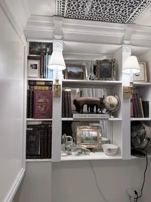 elegant white built-in bookshelf with decorative columns, wall sconces, and ornate ceiling tile in nyc home