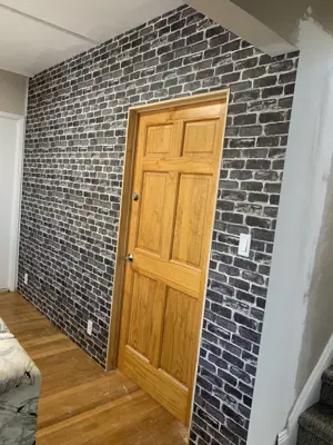 Dark brick-pattern wallpaper installed on accent wall beside a wooden six-panel door in NYC apartment