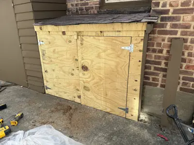 newly built plywood outdoor storage cabinet with hinged doors installed against brick home exterior in nyc