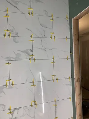 large-format marble-look wall tiles being set with leveling clips during nyc bathroom remodel