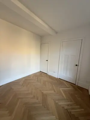 Beautifully finished herringbone hardwood floor pattern in an empty NYC apartment room with white walls