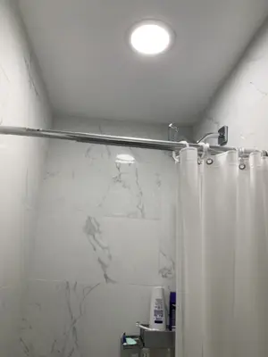renovated bathroom with marble tile walls, curved shower rod, and recessed ceiling light in nyc