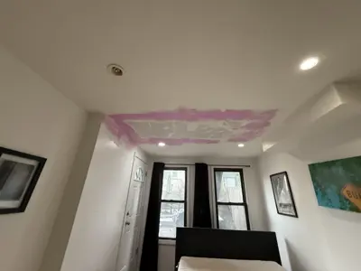Pink drywall joint compound patch drying on bedroom ceiling during NYC painting and repair job