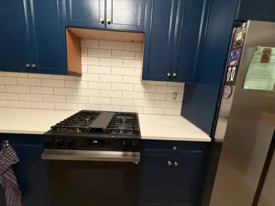 completed kitchen renovation with stainless steel gas range installed among blue cabinets and subway tile backsplash