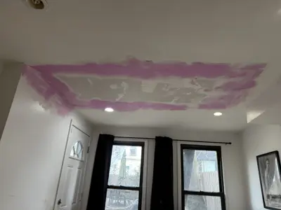 Ceiling drywall repair in progress with pink joint compound applied to patched sections in NYC home