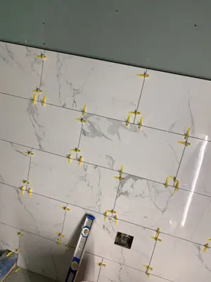 marble-look ceramic tile installation in progress with yellow leveling clips and spacers on floor in nyc