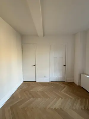 Freshly painted white room with herringbone hardwood floor and clean baseboards in NYC apartment