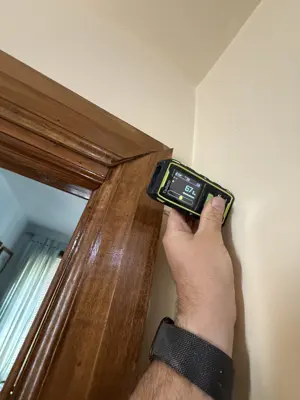 Handyman using a digital stud finder near a door frame during wall repair prep in NYC