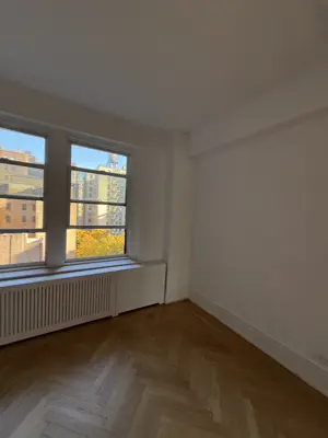 Freshly painted bright white room with herringbone hardwood floors and large windows in NYC apartment