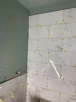 marble-look tile installation in progress on bathroom walls with leveling spacers and green board backing