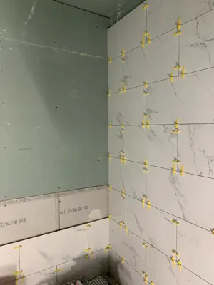 large-format marble-look shower wall tiles with leveling spacers set against green cement board backer in nyc bathroom