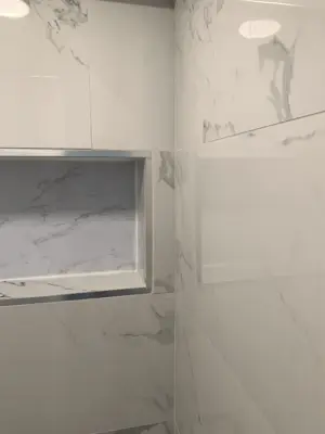 completed marble-look shower tile installation with built-in niche and chrome trim in nyc bathroom