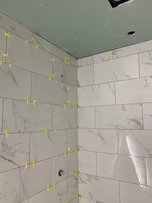 corner shower wall tile installation in progress with marble-look porcelain tiles and yellow leveling spacers in nyc bathroom