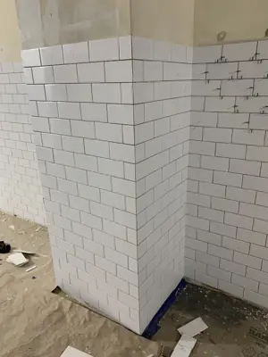 white subway tile installation nearly complete on bathroom column and walls showing clean grout lines and alignment