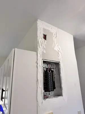 Electrical panel exposed during drywall repair work in a NYC home with spackle applied around breaker box