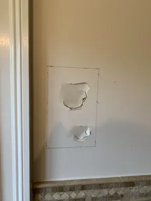 two large holes in drywall marked for repair patch work in nyc bathroom near tile baseboard