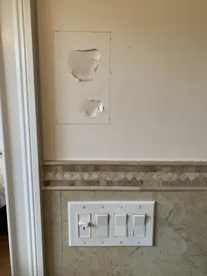two holes in drywall above light switches on tiled bathroom or kitchen wall before repair