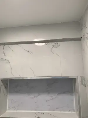 completed marble tile shower enclosure with built-in niche shelf and chrome curtain rod in nyc bathroom