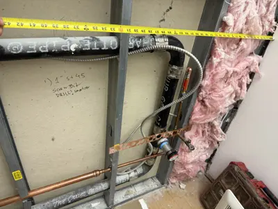 In-wall copper and flexible plumbing pipe rough-in with tape measure during NYC renovation