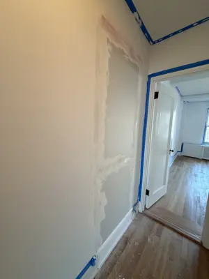 Drywall patch with spackle and blue painter's tape on hallway wall during NYC repair job