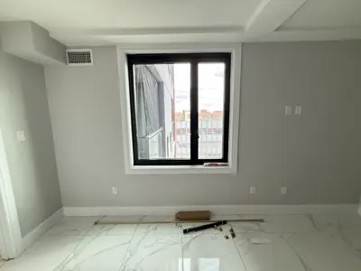 freshly painted light gray room with white trim, marble tile floor, and black window frame in nyc apartment