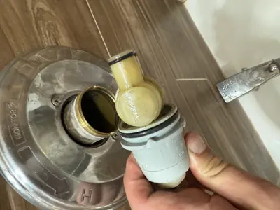 Technician removing worn shower valve cartridge from Moen monitor trim plate during bathroom plumbing repair