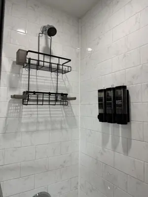 clean marble-tile shower with mounted black wire caddy shelf and soap dispenser in nyc bathroom
