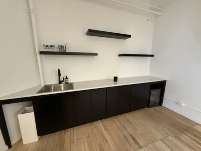 completed modern kitchen area with black cabinets, marble countertop, wall-mounted shelves, and sink in nyc