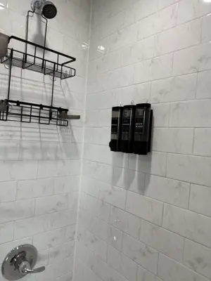 clean modern shower with white marble tile, mounted soap dispensers and black metal caddy installed in nyc bathroom