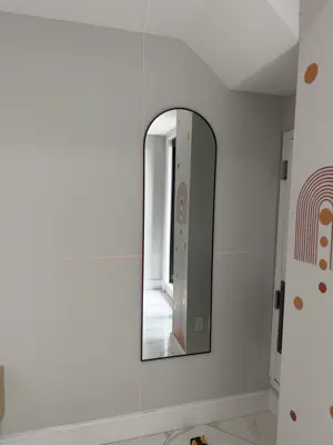 Arch mirror being mounted on a bedroom wall with laser level guide lines visible in NYC