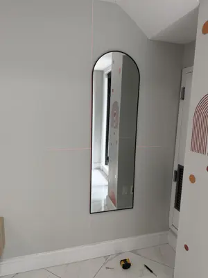 large arch-framed floor mirror mounted on hallway wall with laser level alignment in nyc apartment