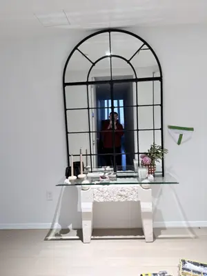 Large arched decorative mirror mounted on a white wall above a console table in a modern NYC apartment