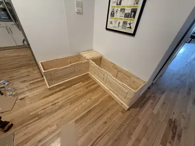 Custom L-shaped wooden bench frame being assembled on hardwood floor in NYC apartment