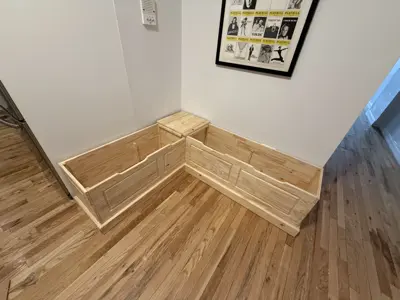 Custom L-shaped wooden storage bench frame in progress in a NYC apartment