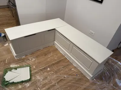Custom L-shaped storage bench being painted white in a NYC kitchen dining area