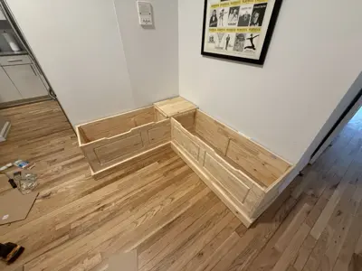 Completed L-shaped wooden bench assembly installed in a NYC apartment corner with hardwood floors