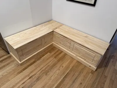 Completed custom L-shaped wooden corner storage bench with lift-top seats in NYC home