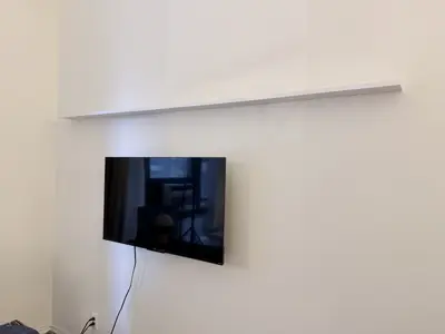 flat screen tv and floating wall shelf mounted on white wall in nyc living room