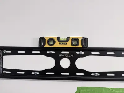 TV wall mount bracket being leveled with DeWalt spirit level during installation process