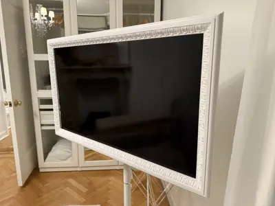 TV mounted in decorative white ornate frame on a floor stand in a NYC apartment living room