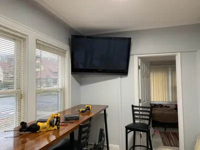 Large flat-screen TV professionally wall-mounted in bright NYC dining area with tools on table