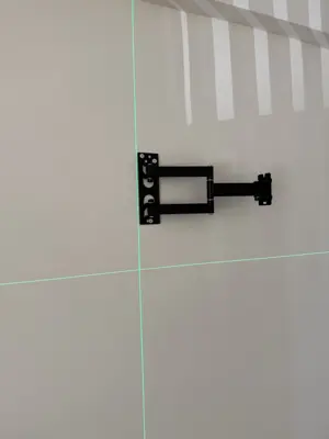 TV wall mount bracket installed on white wall with green laser level lines for precise alignment